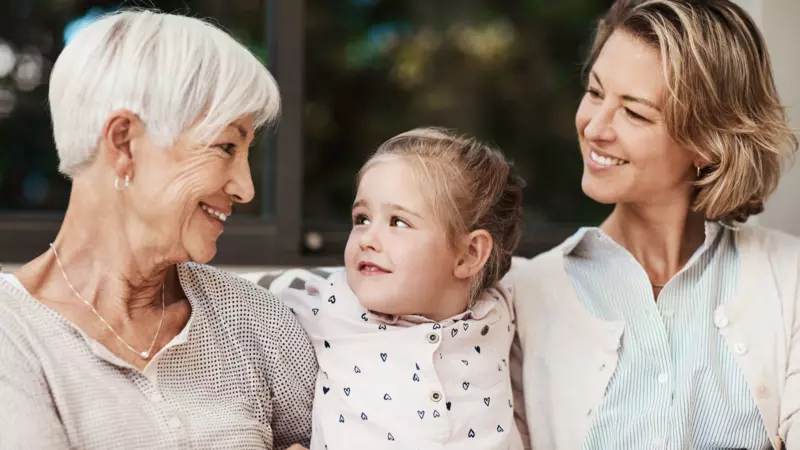 A grandmother, daughter and grand daughter smiling together.  