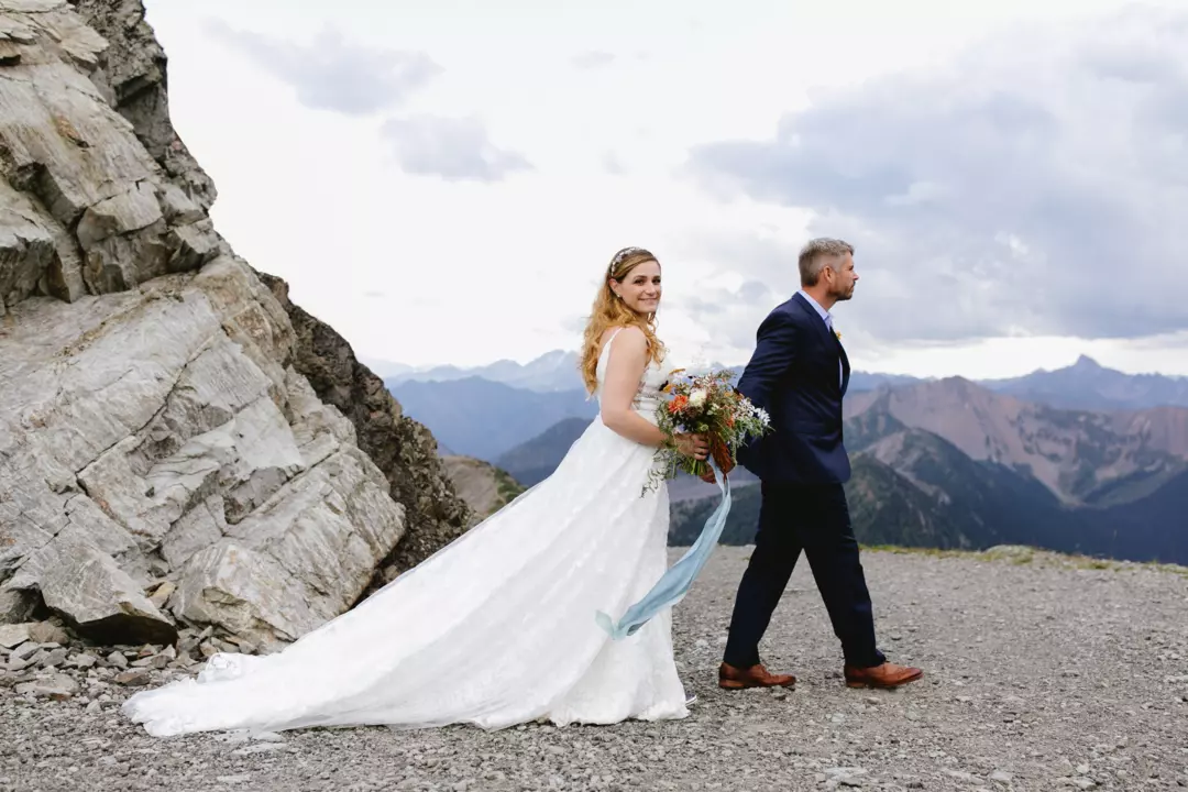 Joanna is in a white wedding dress with her new husband. They are on a mountain. 